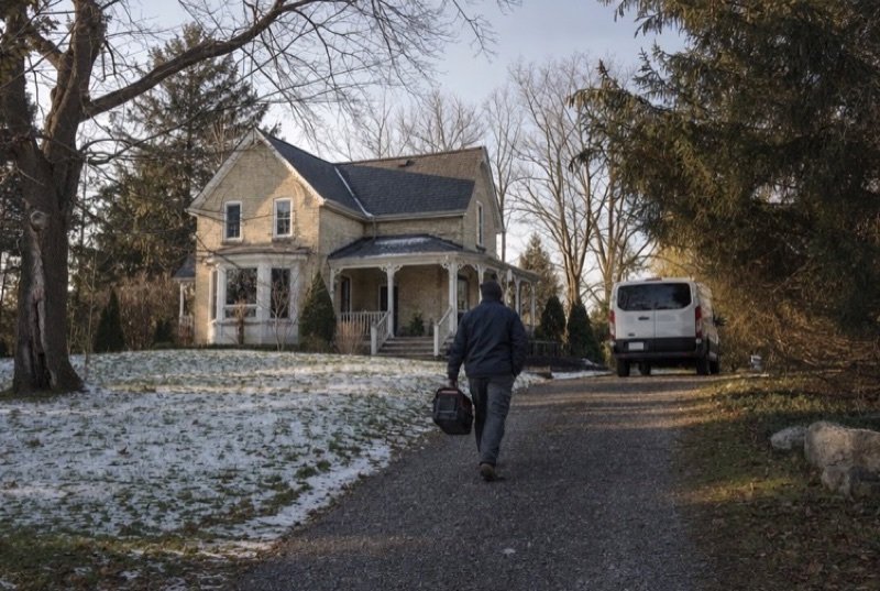 SEO for HVAC, plumbing & electrical: a service technician in a dark jacket carrying a toolbox up a gravel drive to a brick house