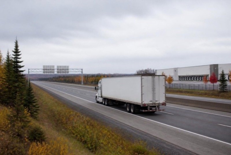 A tractor-trailer with a plain white trailer on a four-lane divided highway through flat valley country